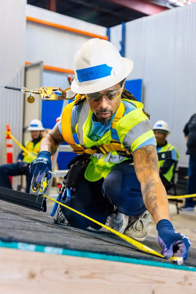 A workforce trainee in full safety equipment measuring a solar panel