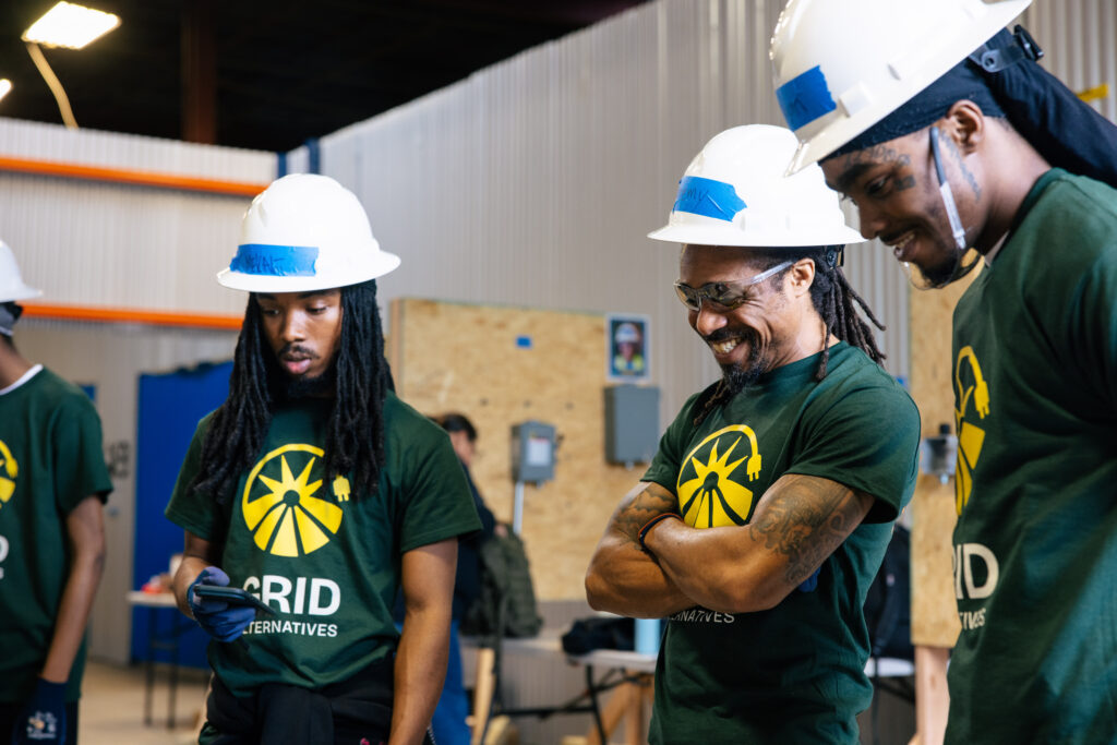 Workers wearing hard hats and green GRID Alternatives shirts smile during training session