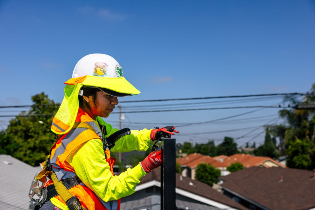 Woman carrying solar panel with safety high visibility equipment on roof to install solar panel