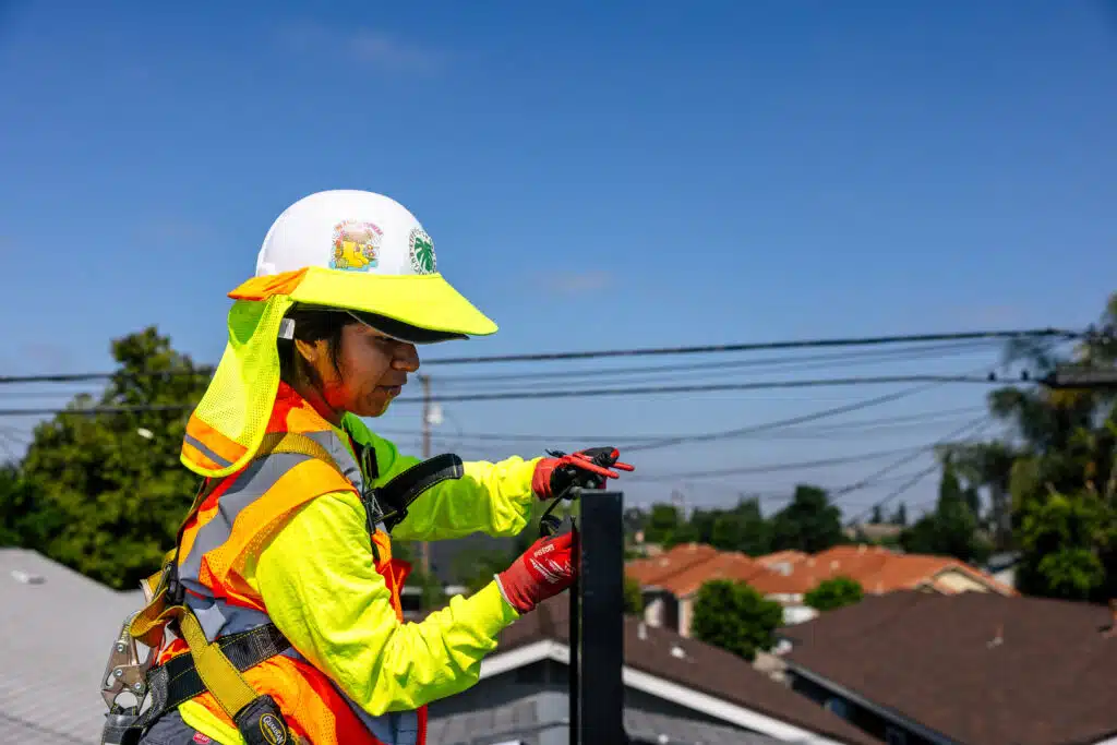 Woman carrying solar panel with safety high visibility equipment on roof to install solar panel