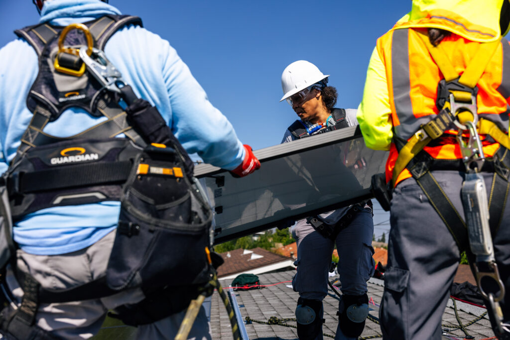 Three installers carrying a solar panel to fit on the roof
