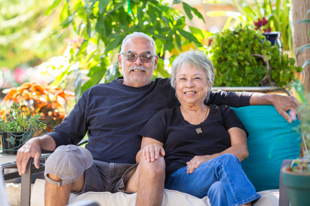 Older couple sitting together on a turquoise chair in a lush garden setting