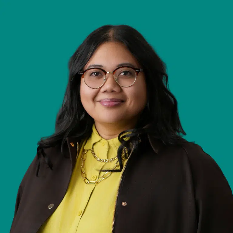 Cindy Corrales, a headshot of a woman wearing a black blazer and yellow blouse. She wears glasses and has dark mid-length hair.